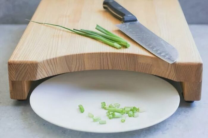 A kitchen knife and chopped green onions on a wooden cutting board with a plate underneath, highlighting useful design.