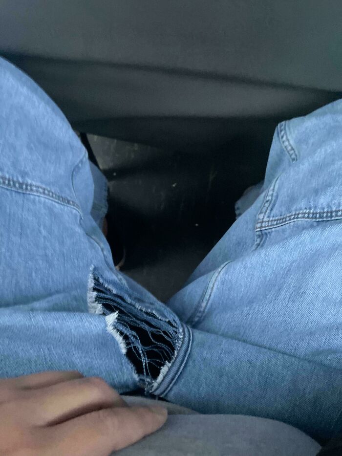 A person's legs in ripped blue jeans, sitting with a tear near the c****h, a common problem needing fixing things.
