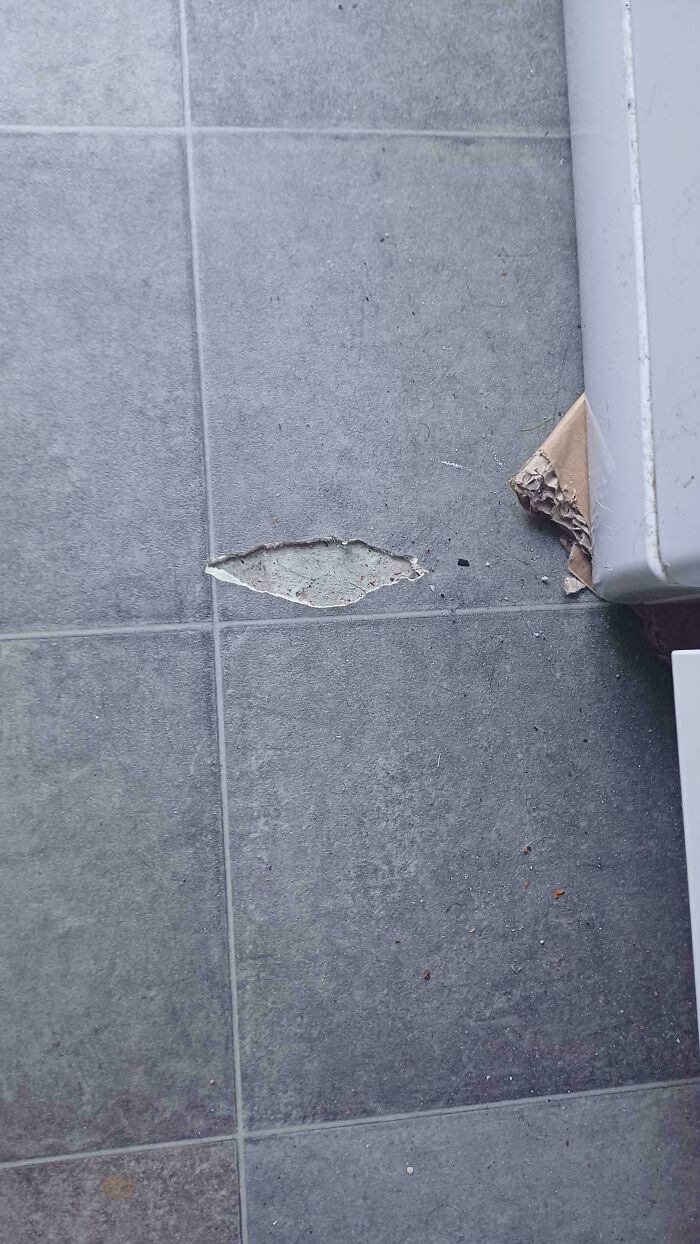 A damaged section of a grey tiled floor where a piece of tile has broken off, indicating a problem needing fixing.