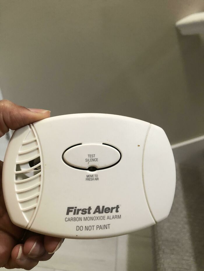 A person's hand holding a First Alert carbon monoxide alarm, presenting a safety device that might need checking or fixing.