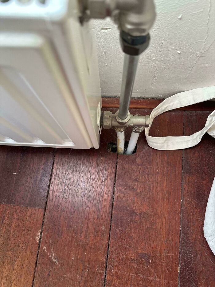A radiator pipe entering a hole in a wooden floor, highlighting a problem that needs fixing things.