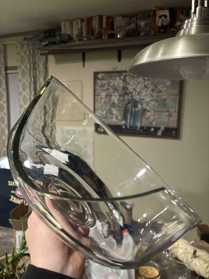 A hand holding a large, clear glass bowl that has a significant chip in its rim, demonstrating a problem needing fixing.