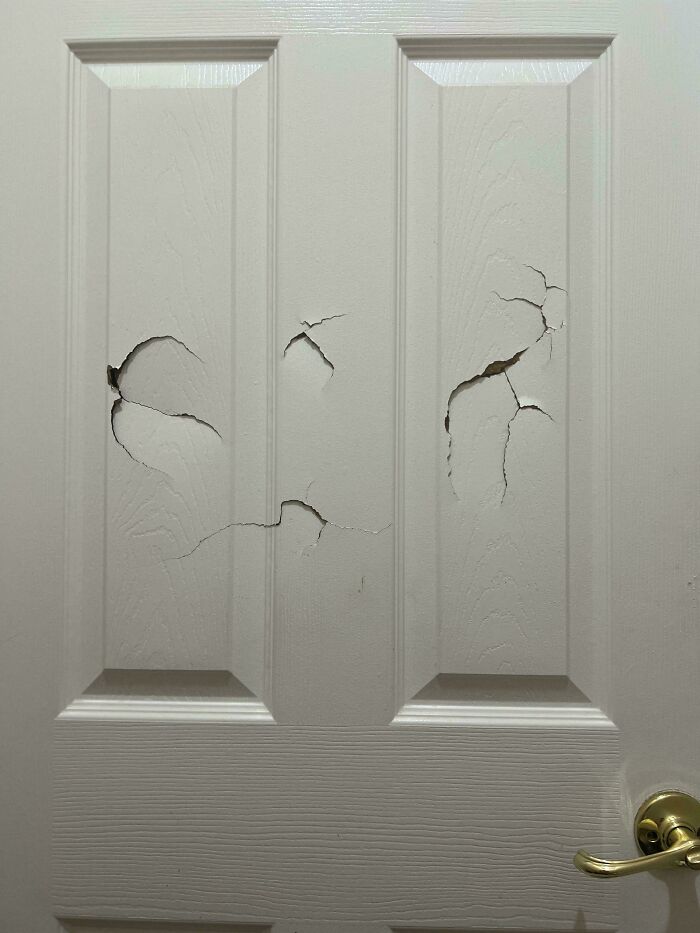 A white door with large cracks and damage across its panels, representing a home maintenance issue requiring help fixing things.