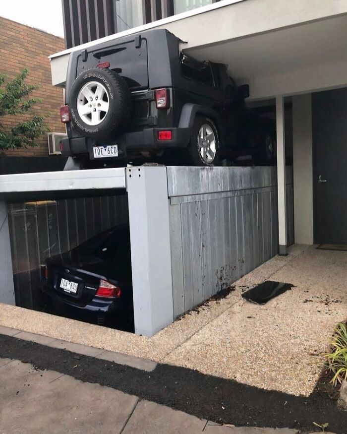 A black Jeep precariously perched on top of a hydraulic garage, a spectacular construction fail.
