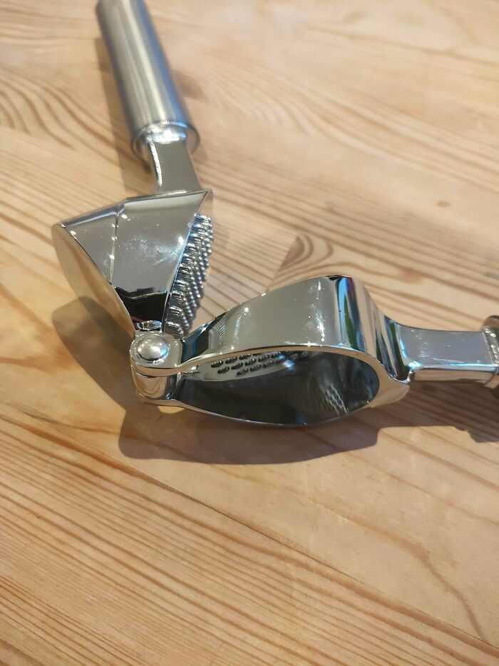 A shiny metal garlic press resting on a wooden surface, ready to help fix cooking problems.