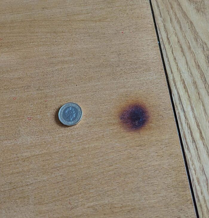 A burnt mark on a wooden table next to a coin for scale, illustrating a problem that needs fixing.