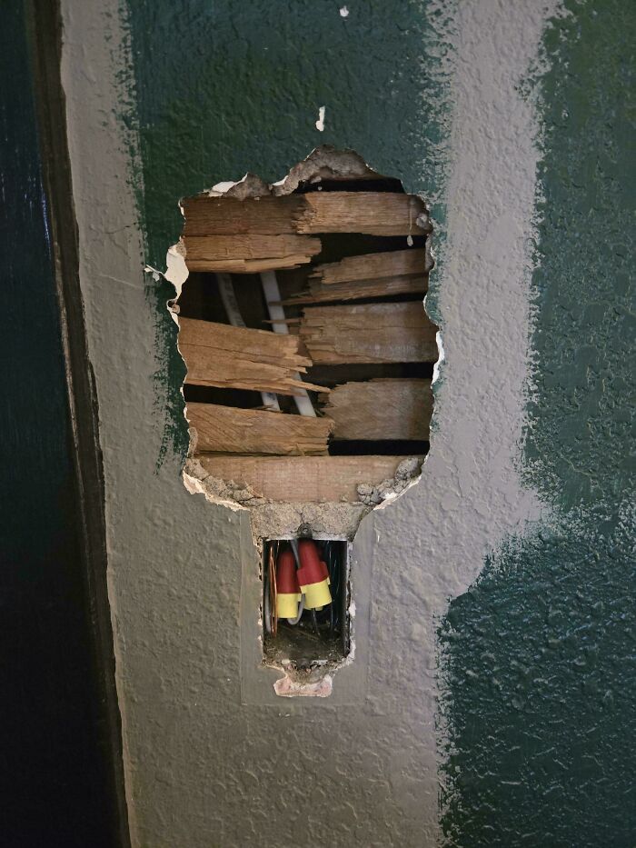 Someone trying to fix things, a damaged wall with exposed wood and electrical wires.