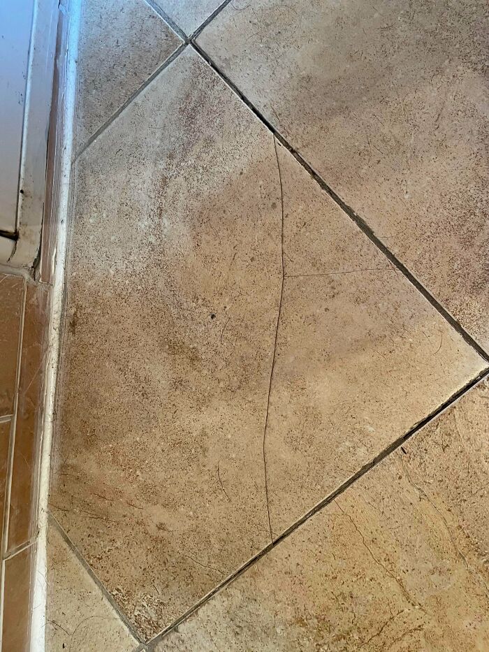 A close-up of a long, thin crack in a light-colored tile floor, a common problem people ask others for help fixing things.