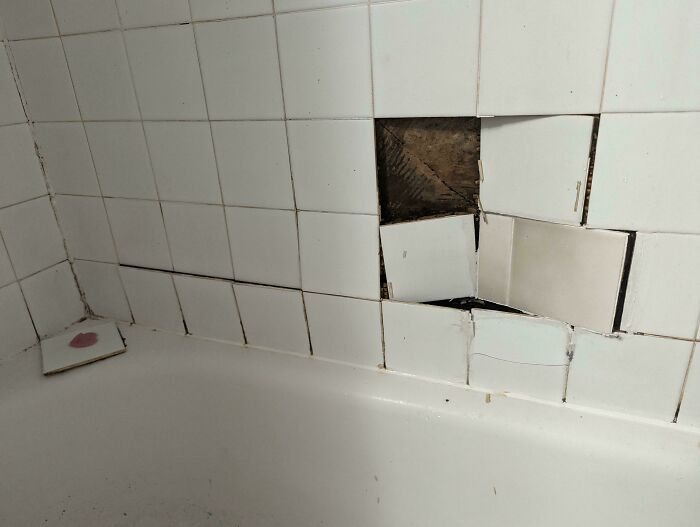 Damaged white tiles in a bathroom, revealing a large hole and broken pieces, a clear problem needing help fixing.