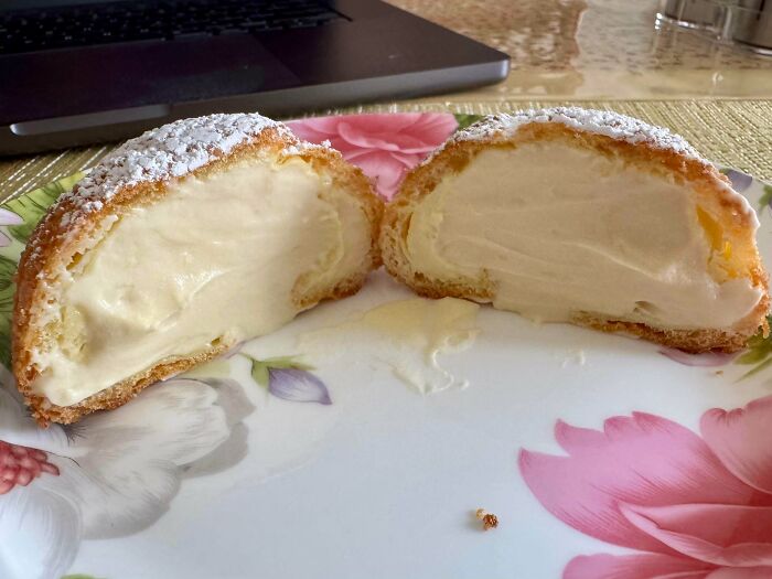 A delicious cream puff cut in half, revealing its creamy filling and a dusting of powdered sugar, proving bakers make amazing treats.