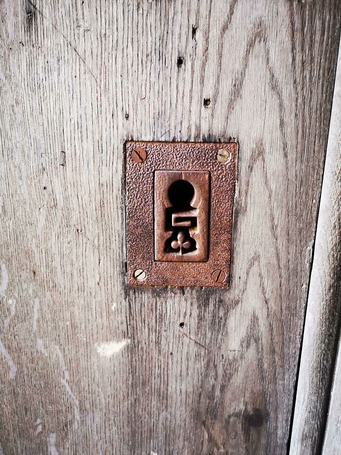 An old wooden door with a keyhole cover that designers transformed into a tiny person, making ordinary things enjoyable.
