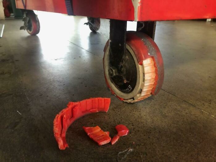 A broken red wheel from a rolling cart, with pieces scattered on the ground, representing a bad day.