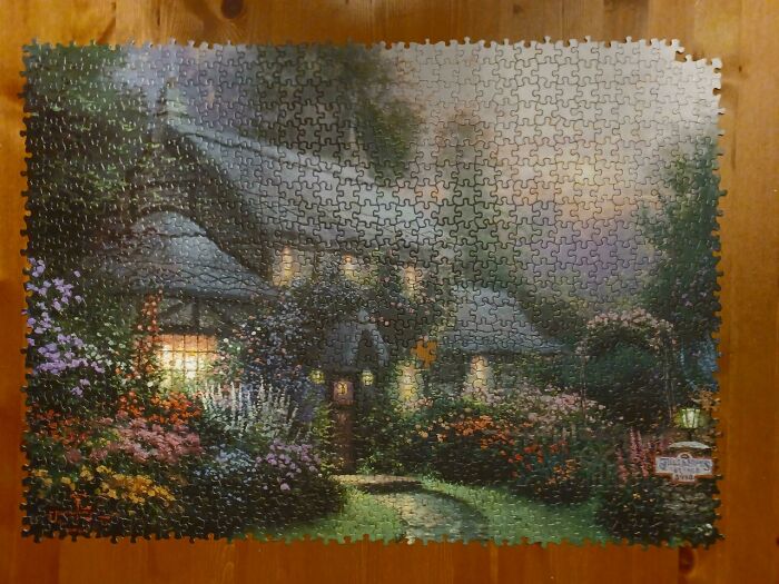 A completed puzzle featuring a quaint cottage with a lit window and colorful garden, depicting a relaxing day.