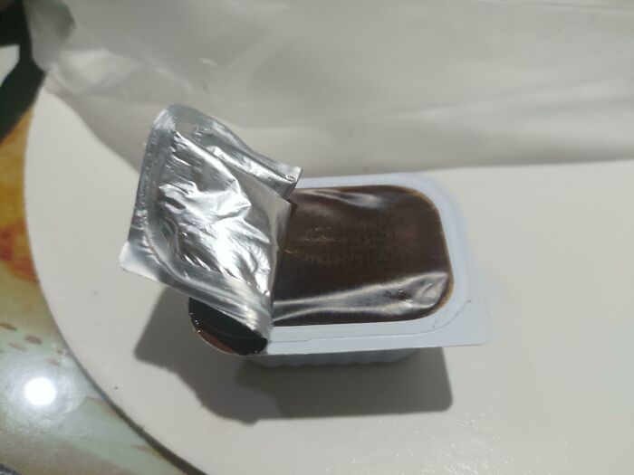 A partially opened chocolate pudding cup, a small disappointment on a worse day.