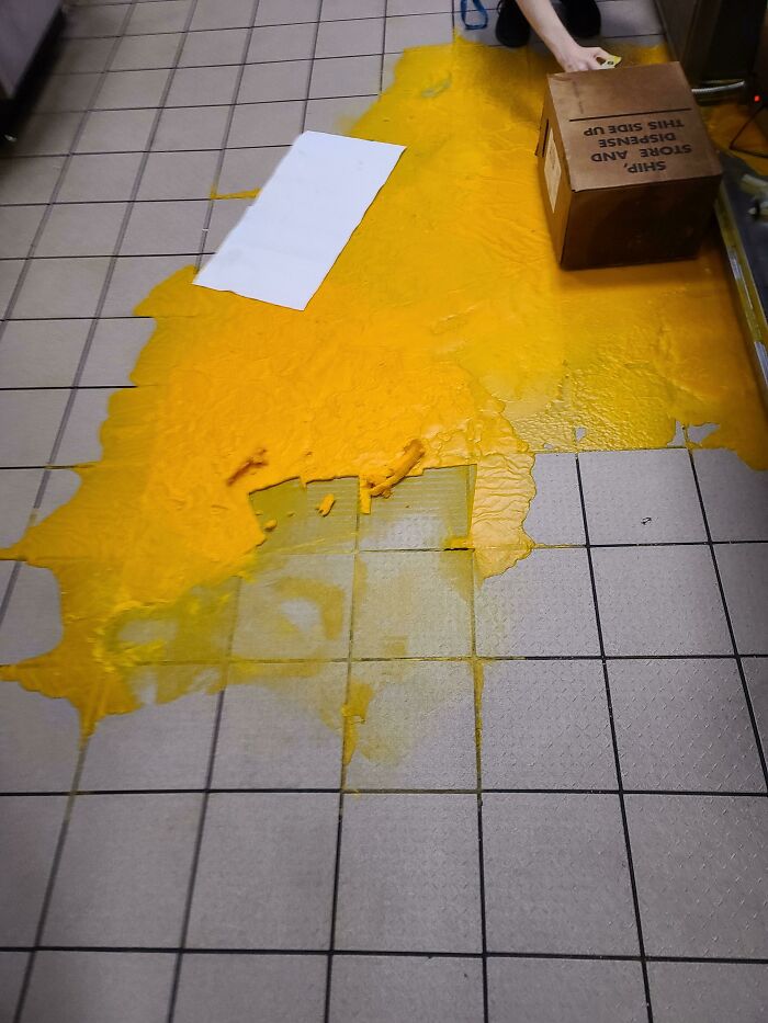 A kitchen floor covered in spilled yellow liquid from a box, a messy day to clean up.
