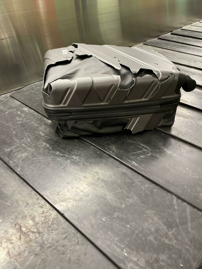 A severely damaged suitcase on a baggage claim conveyor belt, having a worse day than you.