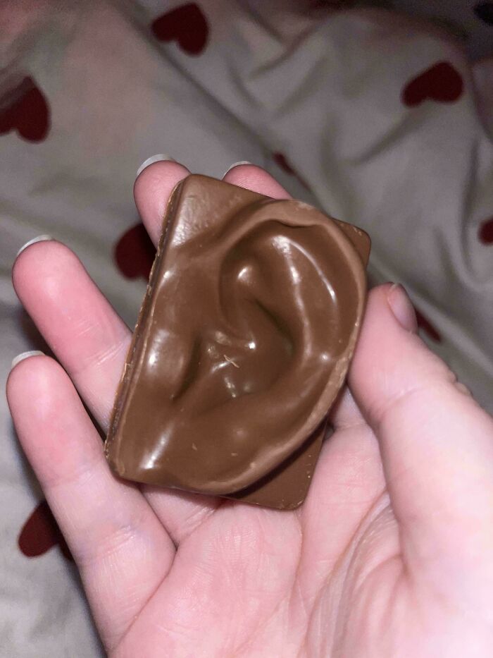 A hand holding a piece of chocolate shaped like an ear, an enjoyable and brilliantly designed ordinary thing.
