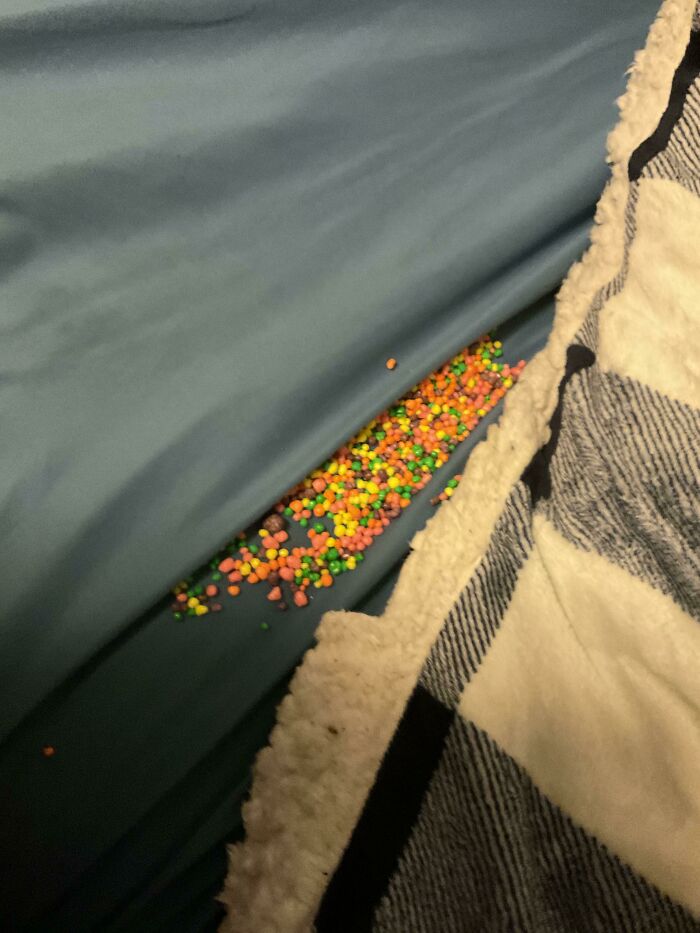 Hundreds of colorful sprinkles scattered across a blue bed sheet, creating a way worse day clean-up.
