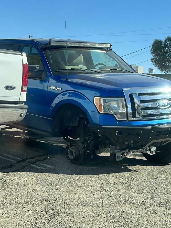 A blue Ford F-150 truck with two wheels missing, a challenging day for the owner.