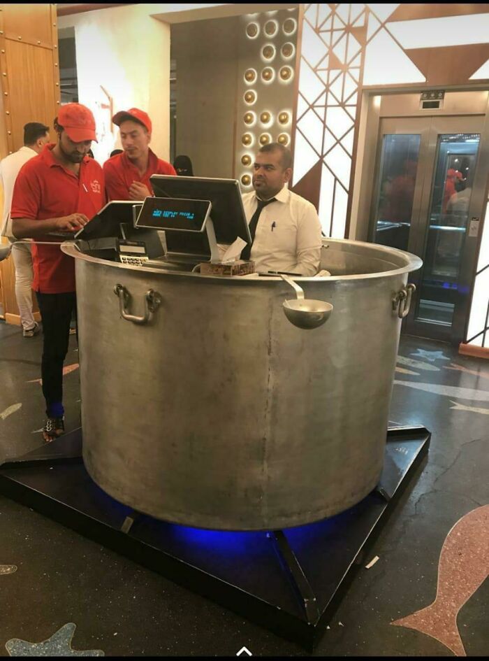 A restaurant host seated inside a giant cooking pot, brilliantly transformed into a unique reception desk, making it more enjoyable.