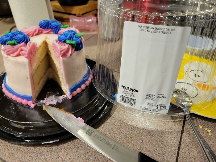 A partially cut small celebration cake with pink and blue icing, illustrating a worse day.