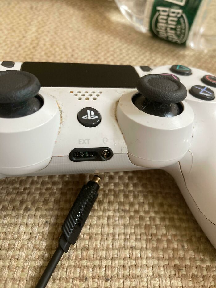 A dirty, well-used PlayStation controller with a broken audio jack, showing a worse day.