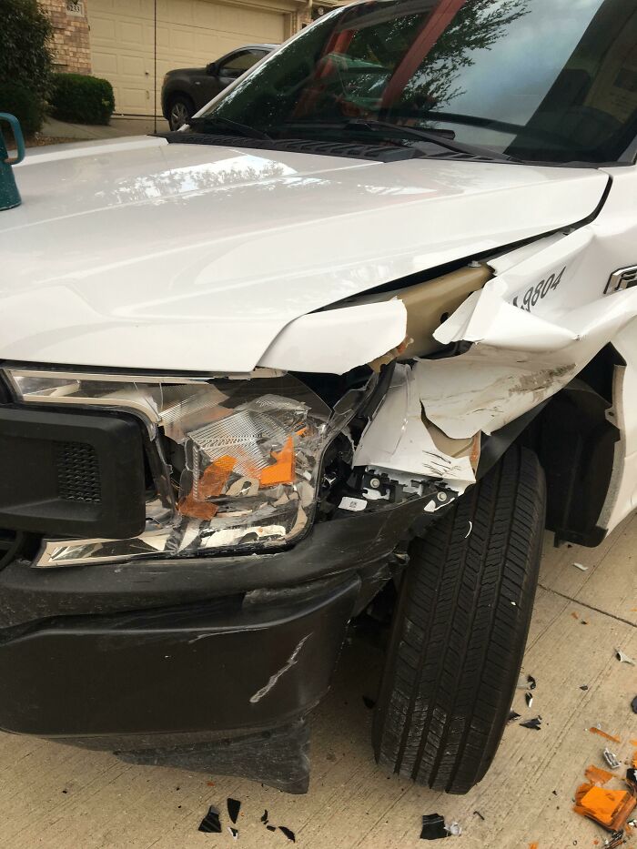 A white truck with a heavily damaged front bumper and headlight, having a worse day than you.