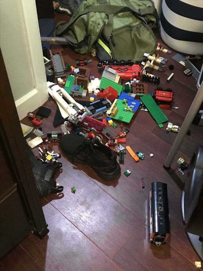 A messy room floor covered with various LEGO pieces, shoes, and a green backpack, creating a chaotic scene.