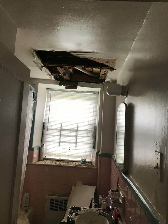 A dilapidated bathroom with a large hole in the ceiling and debris on the floor, showing people having a worse day.