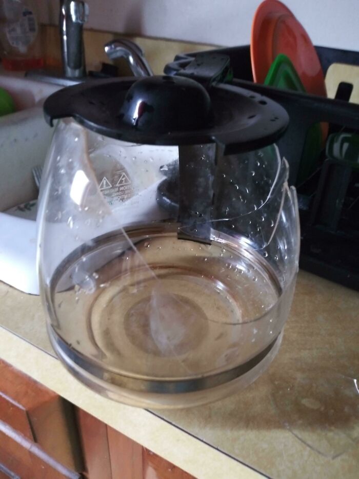 A broken glass coffee pot on a counter, with a sink and dishes in the background, showing someone having a bad day.