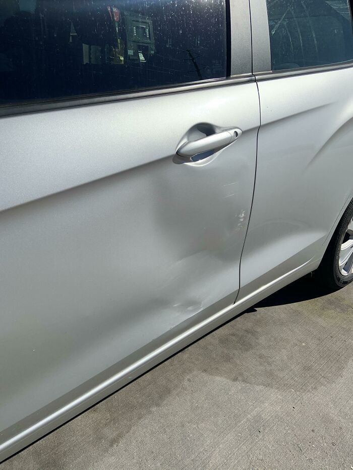 A person having a worse day, a silver car with a noticeable dent on its side door.