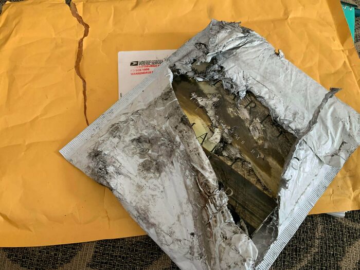 A damaged, ripped open mail package lying on a yellow envelope, illustrating someone having a way worse day.