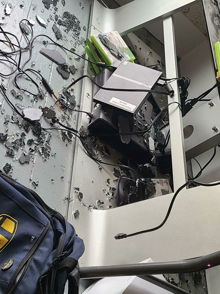 Shattered glass and gaming consoles like an Xbox and PlayStation on a shelf, signifying someone having a way worse day.