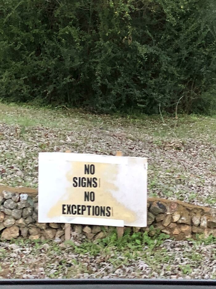 A white sign in a field reads NO SIGNS NO EXCEPTIONS, a hilariously failed sign.