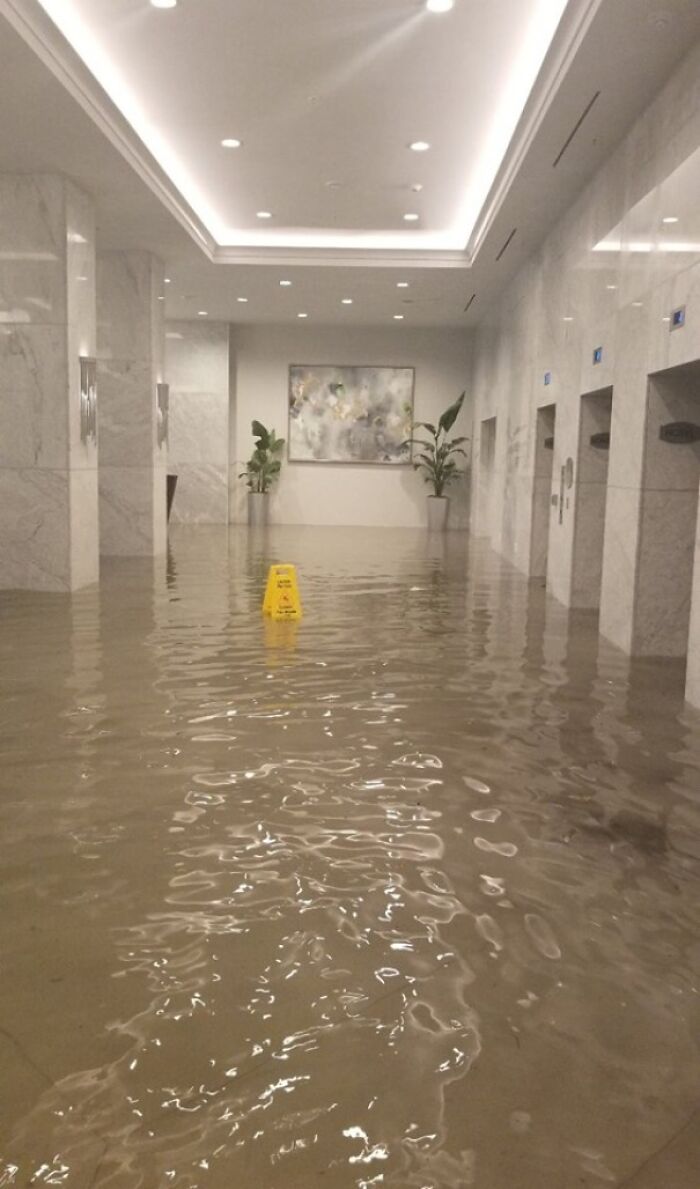 A hilariously failed sign, a yellow wet floor sign in a building lobby completely flooded with water.