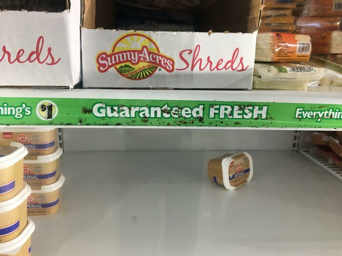 A hilariously failed sign in a store, claiming Guaranteed FRESH above a rusty and dirty shelf.