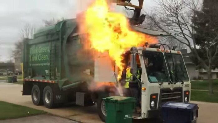 A person having a worse day, a garbage truck engulfed in flames on a street.