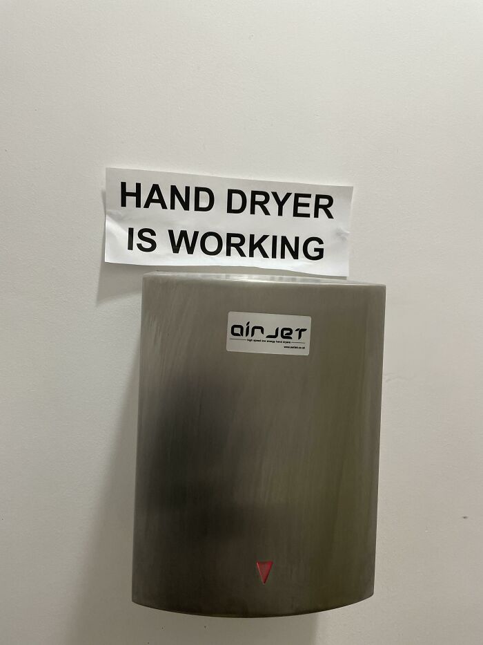 A hand dryer with a sign above it stating HAND DRYER IS WORKING, hilariously failed at its intention.