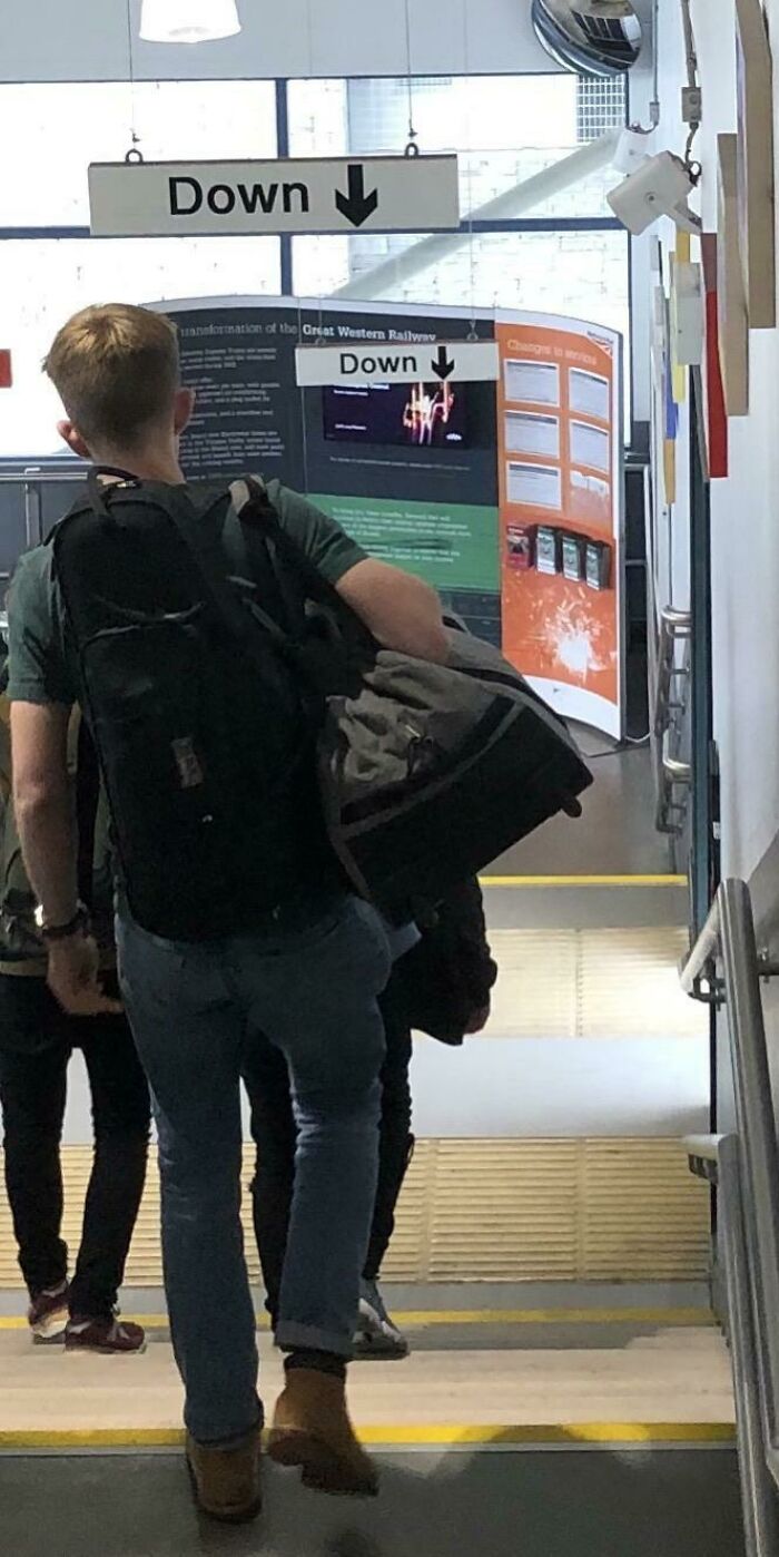 A man walking up stairs past multiple signs that hilariously failed by pointing 'Down' at a Great Western Railway station.