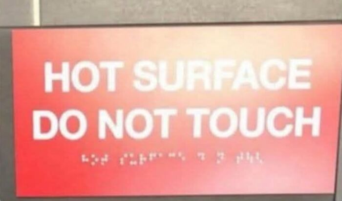 A hilariously failed red sign with white text says HOT SURFACE DO NOT TOUCH, with braille below it.