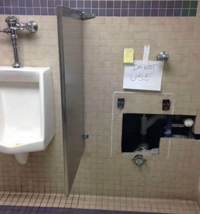A hilariously failed sign reading DO NOT USE next to a broken urinal with exposed pipes in a public restroom.