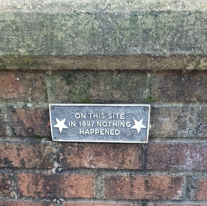 A plaque on a brick wall reads On This Site In 1897 Nothing Happened, a hilariously failed sign of historical significance.