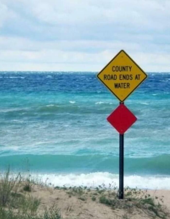 A sign by the ocean hilariously states County Road Ends At Water, demonstrating a sign that failed its purpose.