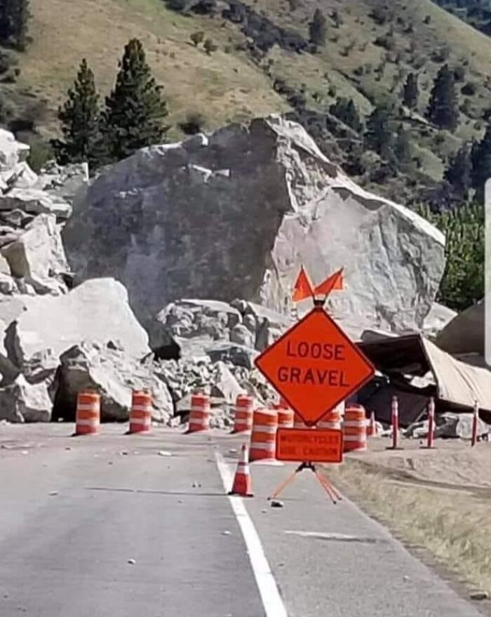 A hilariously failed sign warns of loose gravel as large boulders cover the road.