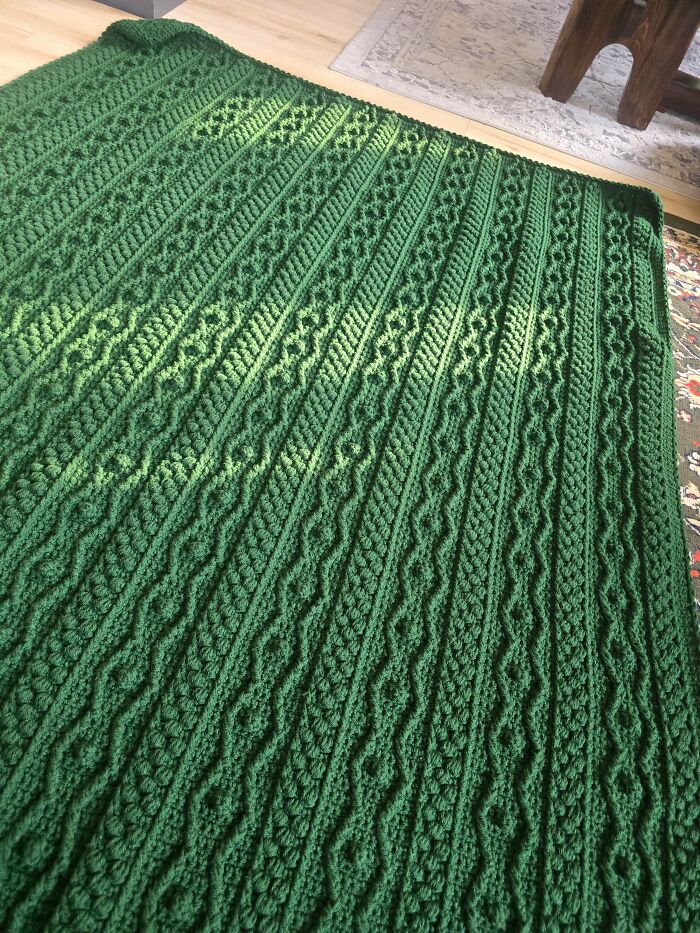 Textured green crochet blanket with cable and diamond patterns on wooden floor
