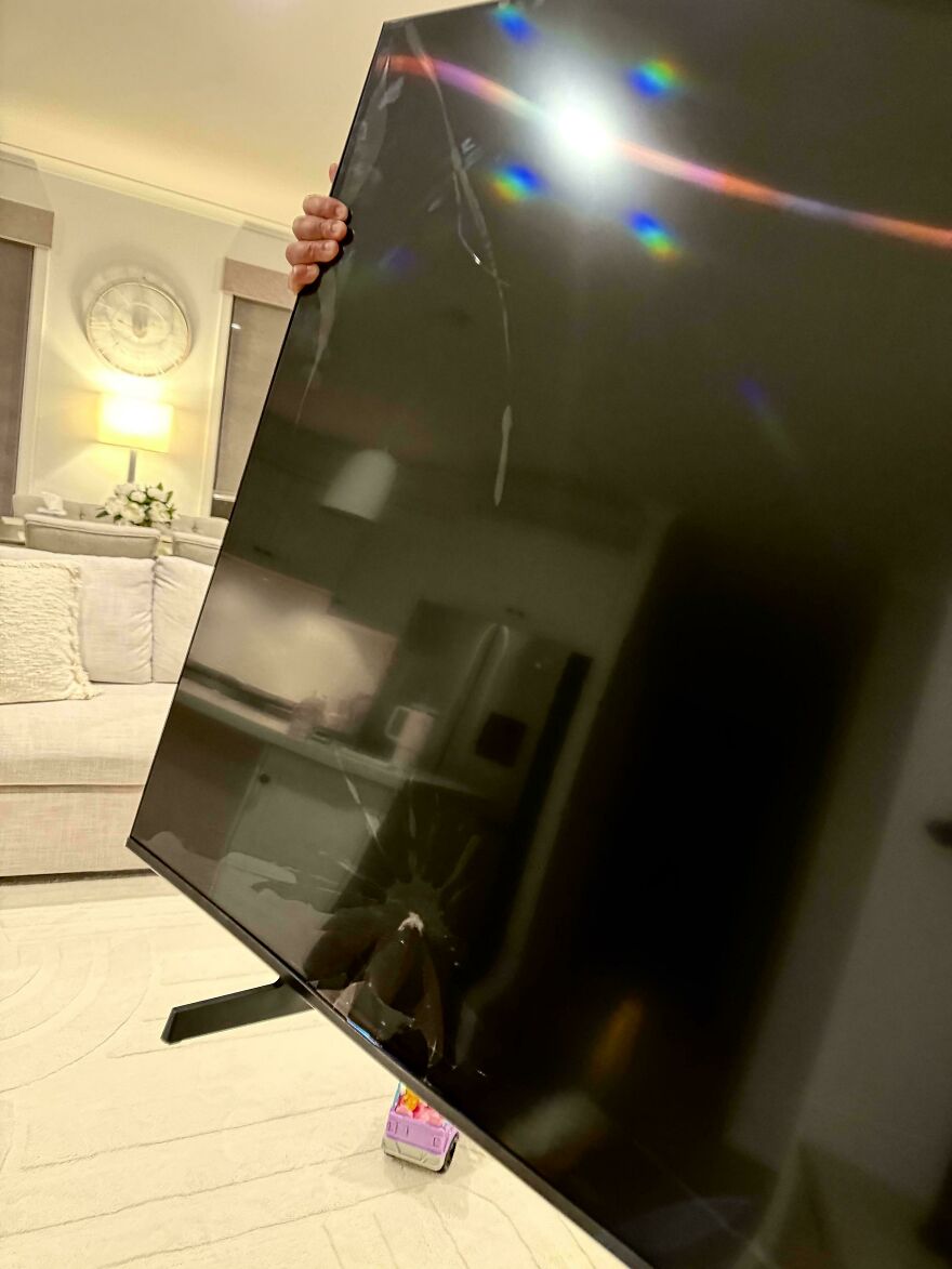A large television with a cracked screen being held upright, an expensive accident showing damage.