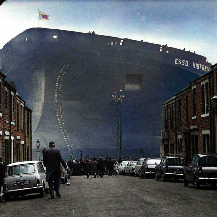 The colossal Esso Hibernia ship towering over a street with small buildings and cars, a striking size comparison.