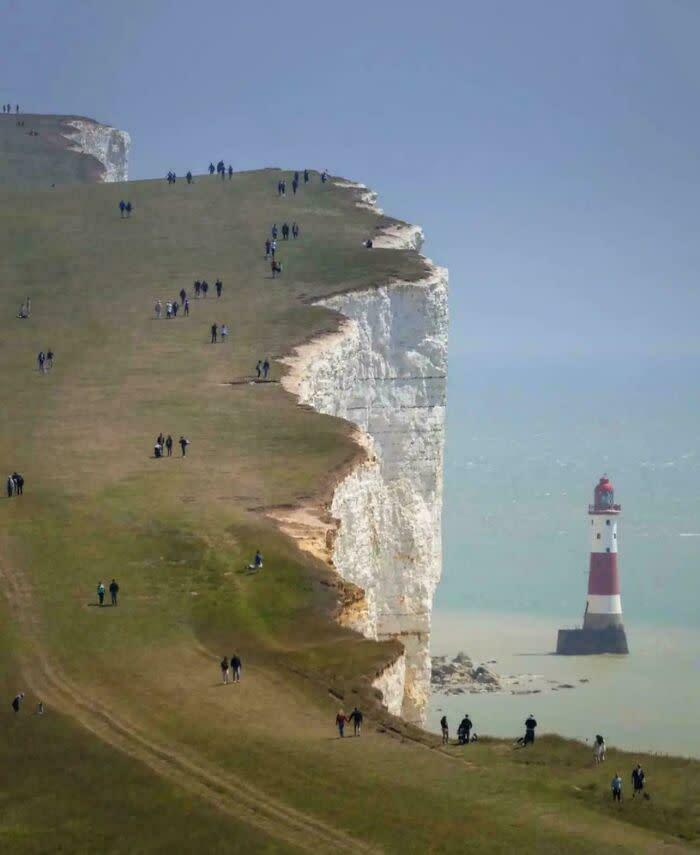 A small lighthouse at the base of vast white cliffs, demonstrating a dramatic size comparison and true scale.