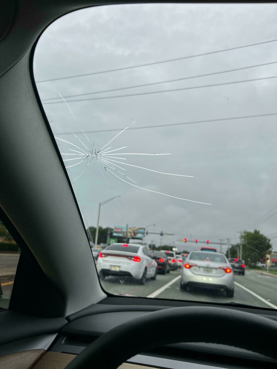 A cracked car windshield with an expensive mistake and accident, showing traffic in the background on a cloudy day.