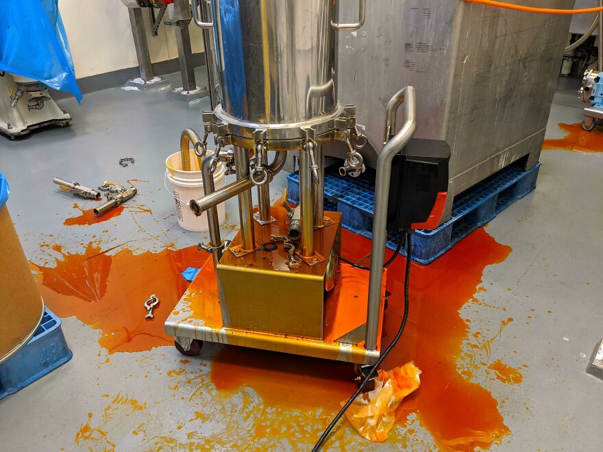 Industrial machinery with a significant spill of orange liquid on the factory floor, an expensive mistake and accident.
